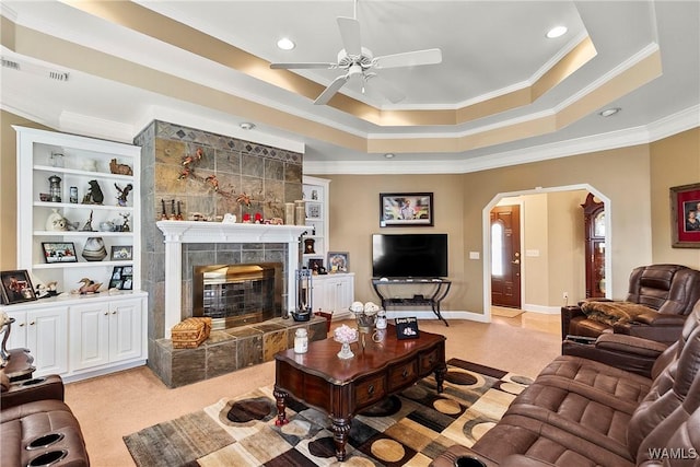 living room with visible vents, arched walkways, a tiled fireplace, ornamental molding, and a tray ceiling