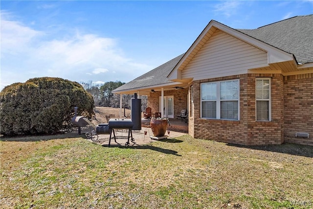 rear view of property with roof with shingles, a yard, brick siding, a patio, and ceiling fan