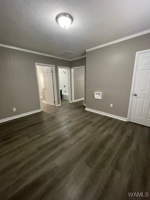 empty room with dark wood-type flooring, ornamental molding, a textured ceiling, and baseboards