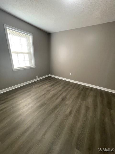 empty room featuring dark wood-style floors, a textured ceiling, and baseboards