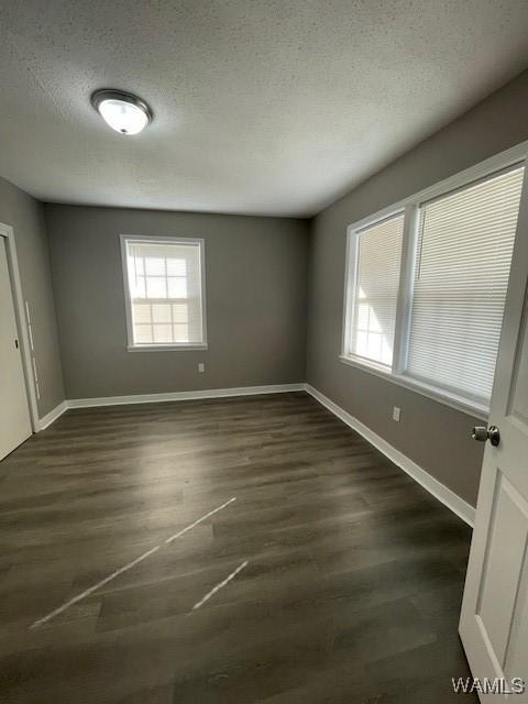 unfurnished room with baseboards, dark wood finished floors, and a textured ceiling