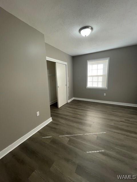 unfurnished bedroom with dark wood-style floors, a textured ceiling, a closet, and baseboards