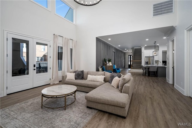 living area with french doors, visible vents, wood finished floors, a chandelier, and stairs