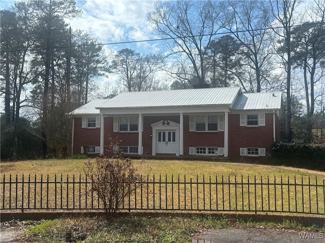 split foyer home with a fenced front yard, metal roof, a front lawn, a porch, and brick siding