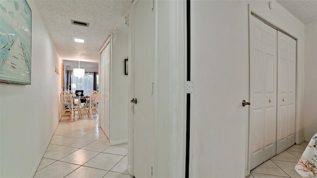 hall with a textured ceiling and light tile flooring