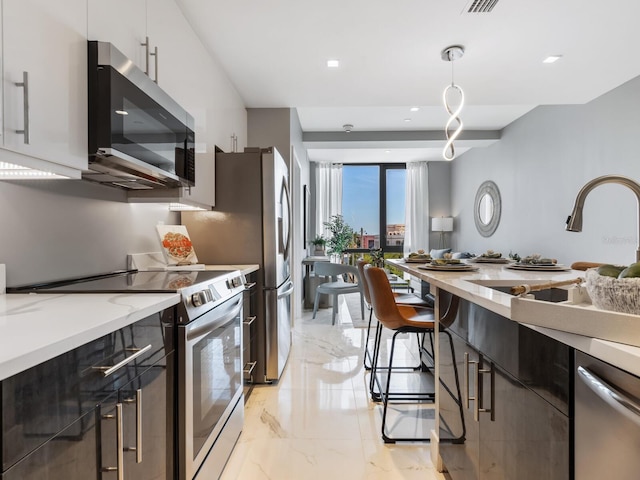 kitchen with light stone counters, stainless steel appliances, sink, white cabinets, and hanging light fixtures