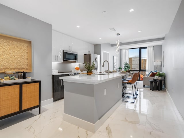 kitchen with sink, an island with sink, appliances with stainless steel finishes, decorative light fixtures, and white cabinetry