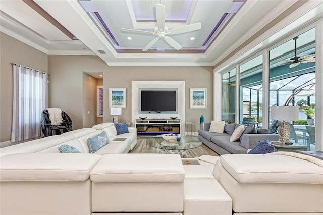 living room featuring a raised ceiling, ceiling fan, and ornamental molding