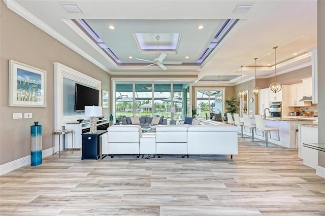 living room with light hardwood / wood-style floors, a tray ceiling, ornamental molding, and ceiling fan