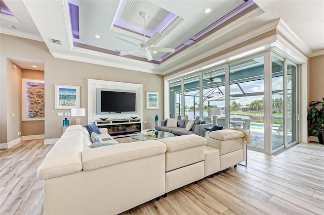 living room featuring a tray ceiling, ceiling fan, ornamental molding, and light hardwood / wood-style flooring