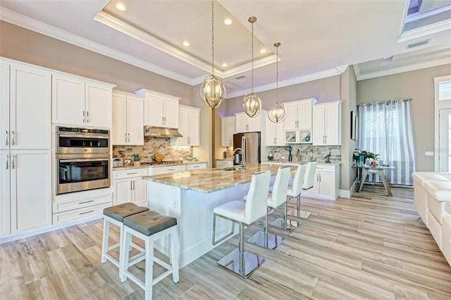 kitchen featuring a breakfast bar, stainless steel appliances, white cabinets, a center island with sink, and a raised ceiling