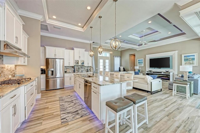 kitchen featuring a tray ceiling, a kitchen island with sink, appliances with stainless steel finishes, and ceiling fan with notable chandelier