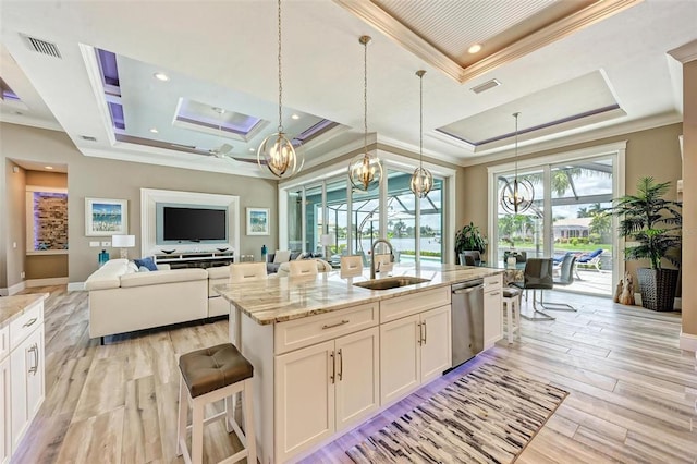 kitchen with a kitchen island with sink, light stone counters, hanging light fixtures, white cabinets, and a tray ceiling