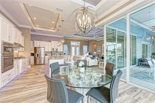 dining room with a raised ceiling, light hardwood / wood-style floors, ornamental molding, and ceiling fan with notable chandelier