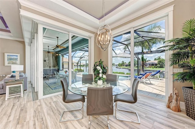 dining area with ceiling fan with notable chandelier, ornamental molding, a water view, a tray ceiling, and light wood-type flooring