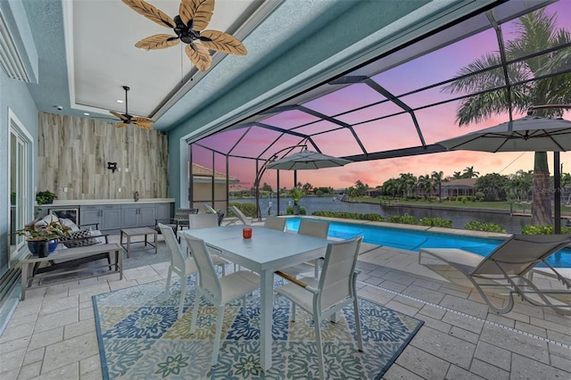 patio terrace at dusk with outdoor lounge area, ceiling fan, a lanai, and a water view