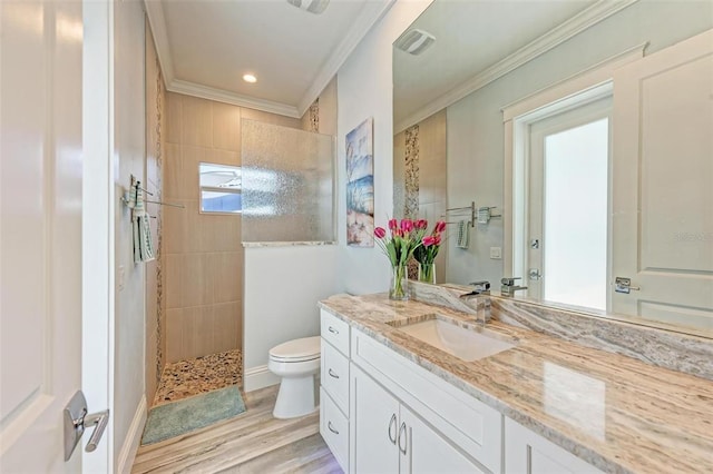 bathroom with vanity, a tile shower, wood-type flooring, toilet, and crown molding