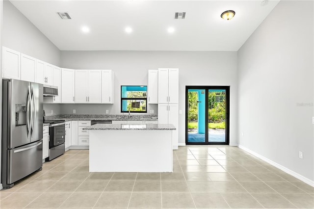 kitchen featuring light stone countertops, white cabinetry, light tile flooring, appliances with stainless steel finishes, and a kitchen island