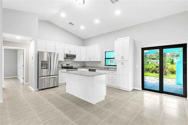 kitchen featuring light tile floors, a kitchen island, white cabinets, appliances with stainless steel finishes, and light stone countertops