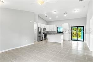 kitchen featuring light tile floors, stove, stainless steel refrigerator with ice dispenser, white cabinetry, and a center island