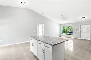 kitchen featuring lofted ceiling, a kitchen island, light tile floors, light stone countertops, and white cabinets