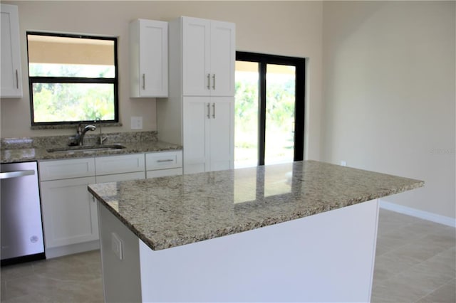 kitchen featuring stainless steel dishwasher, light tile floors, light stone countertops, white cabinetry, and sink