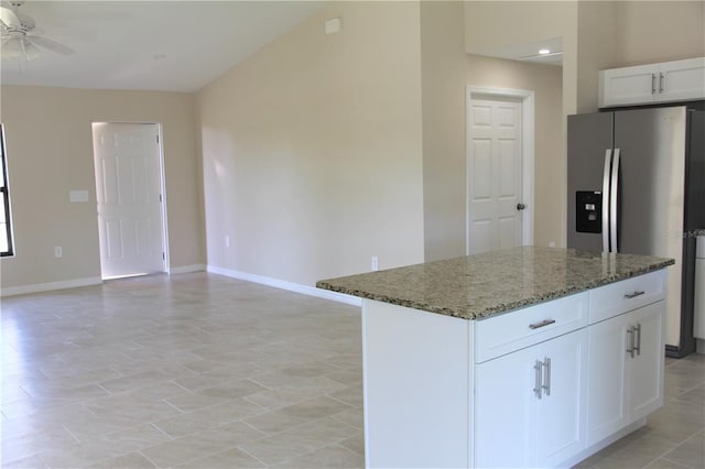 kitchen featuring white cabinetry, ceiling fan, light tile flooring, dark stone counters, and a kitchen island