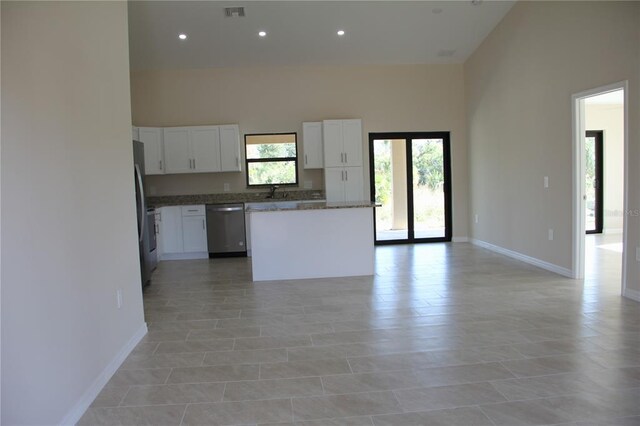 kitchen with stainless steel appliances, light tile floors, a center island, a towering ceiling, and white cabinetry