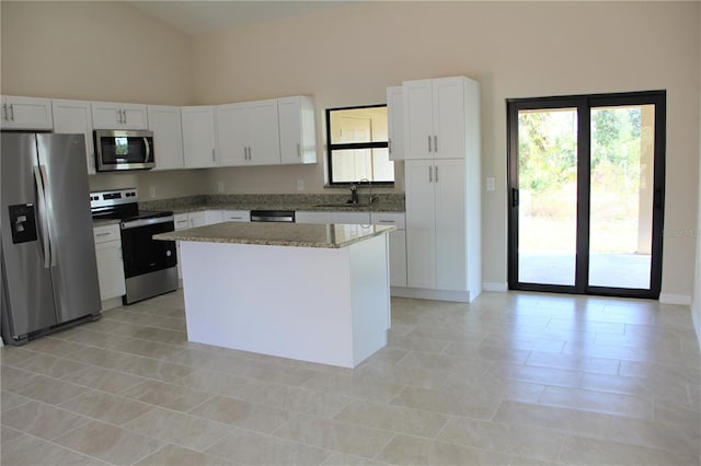 kitchen featuring light stone counters, appliances with stainless steel finishes, high vaulted ceiling, white cabinetry, and a center island