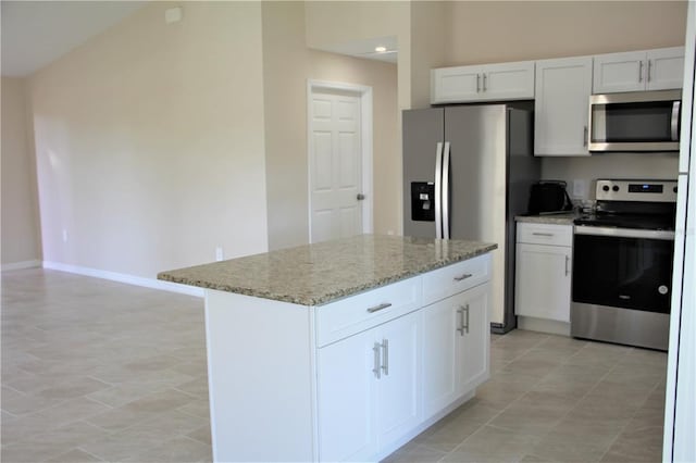 kitchen with appliances with stainless steel finishes, light tile floors, white cabinets, light stone counters, and a kitchen island