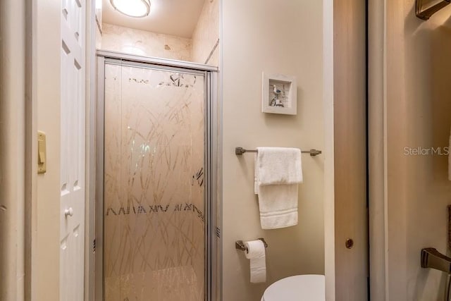 bathroom featuring a shower with door and toilet