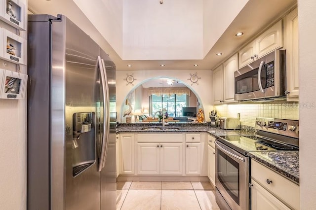 kitchen with sink, tasteful backsplash, light tile patterned floors, dark stone counters, and stainless steel appliances