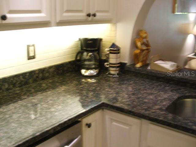 kitchen featuring stainless steel dishwasher, dark stone countertops, white cabinets, and backsplash