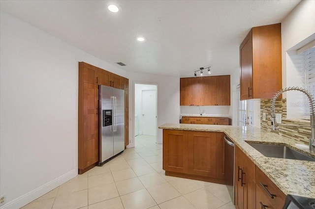 kitchen featuring decorative backsplash, sink, light stone countertops, appliances with stainless steel finishes, and light tile patterned floors