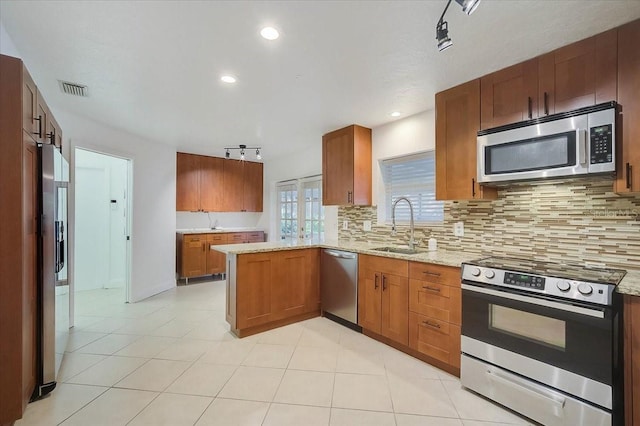 kitchen with light stone countertops, appliances with stainless steel finishes, decorative backsplash, sink, and kitchen peninsula