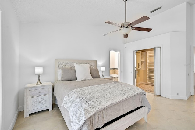 bedroom with a spacious closet, connected bathroom, a closet, light tile patterned flooring, and ceiling fan