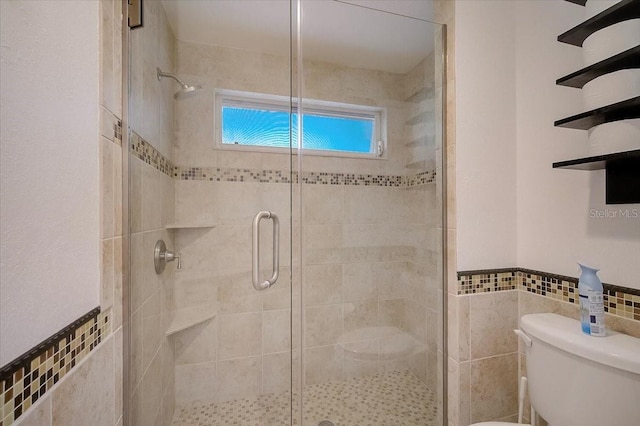 bathroom featuring a shower with shower door, tile walls, and toilet