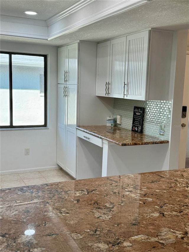 kitchen with dark stone counters, decorative backsplash, crown molding, a textured ceiling, and light tile patterned floors