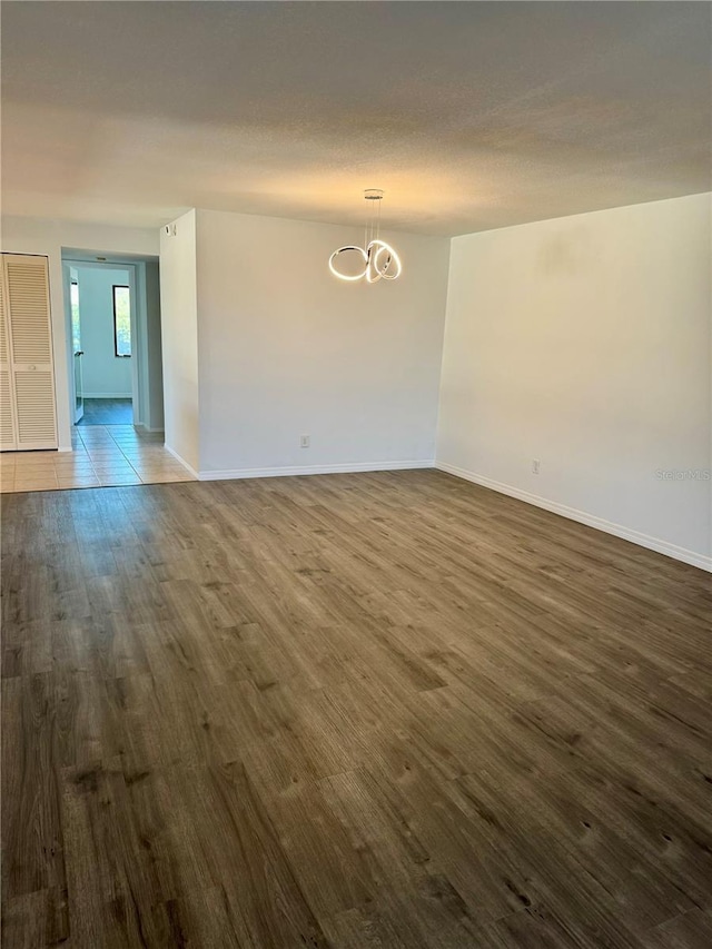 unfurnished room featuring an inviting chandelier and dark wood-type flooring