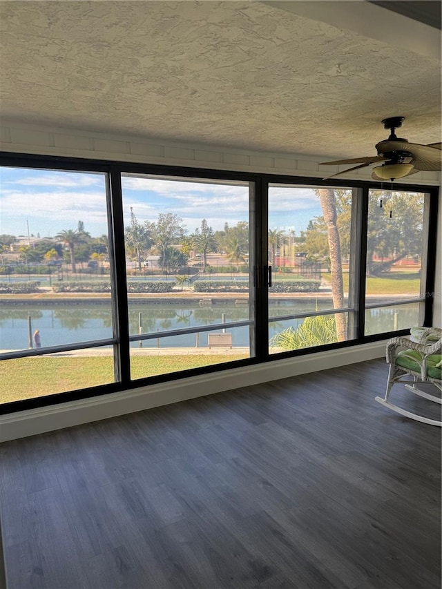 unfurnished sunroom with ceiling fan, a water view, and plenty of natural light