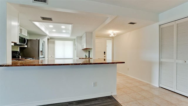 kitchen with kitchen peninsula, dark stone counters, white cabinets, and stainless steel appliances