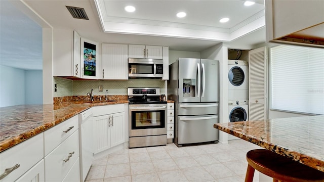 kitchen with white cabinetry, stacked washer / dryer, backsplash, stainless steel appliances, and a raised ceiling