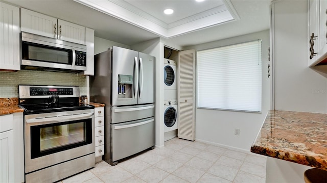 kitchen with tasteful backsplash, stacked washer / dryer, white cabinets, ornamental molding, and appliances with stainless steel finishes