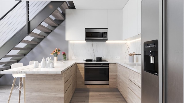 kitchen with kitchen peninsula, white cabinetry, stainless steel appliances, light wood-type flooring, and decorative backsplash