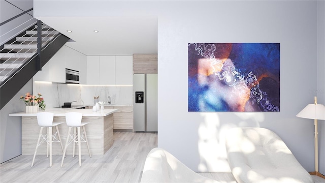 kitchen with white fridge with ice dispenser, light hardwood / wood-style floors, tasteful backsplash, a breakfast bar area, and white cabinetry