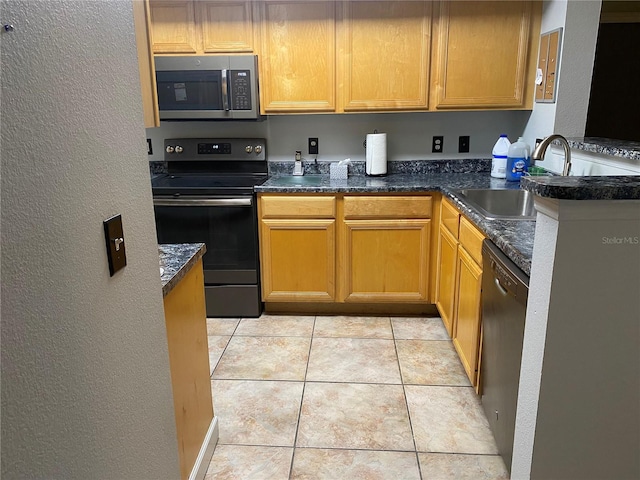 kitchen with light tile floors, dark stone counters, sink, and stainless steel appliances