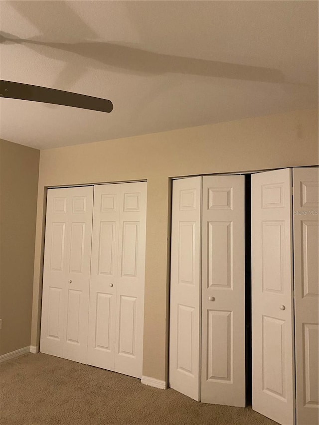 unfurnished bedroom with two closets, carpet flooring, and ceiling fan