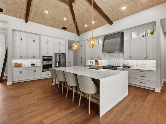 kitchen with wood ceiling, pendant lighting, stainless steel appliances, a kitchen island with sink, and wall chimney range hood