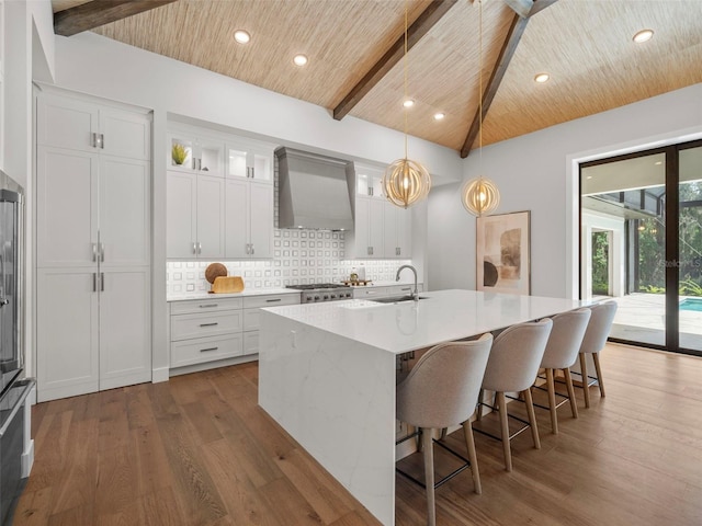 kitchen with wall chimney exhaust hood, sink, wooden ceiling, a kitchen island with sink, and white cabinets