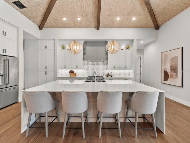 kitchen with hanging light fixtures, high quality fridge, white cabinets, wooden ceiling, and a large island with sink